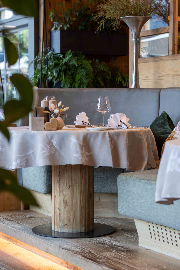 Stilvoll gedeckter Tisch im Restaurant des DER ENGEL im Tannheimertal. Hochwertige Naturmaterialien, gemütliche Sitznischen, frisches Grün und liebevolle Dekoration schaffen eine einladende Atmosphäre für genussvolle Momente in alpinem Ambiente.