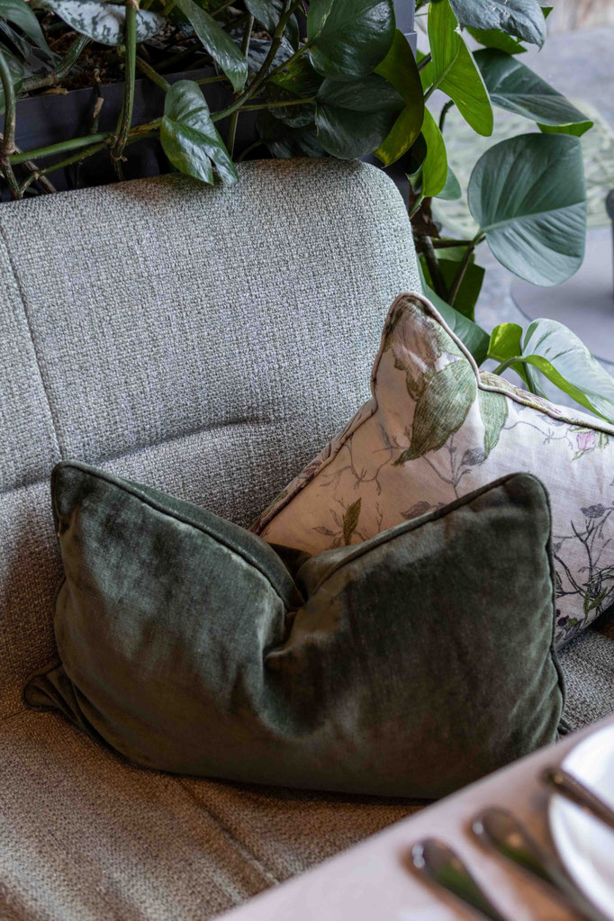 Gemütliche Sitzbank mit dekorativen Kissen und üppigem Pflanzengrün im Restaurant des DER ENGEL im Tannheimertal. Hochwertige Stoffe, natürliche Farben und liebevolle Details schaffen eine stilvolle Atmosphäre zum Entspannen und Genießen.