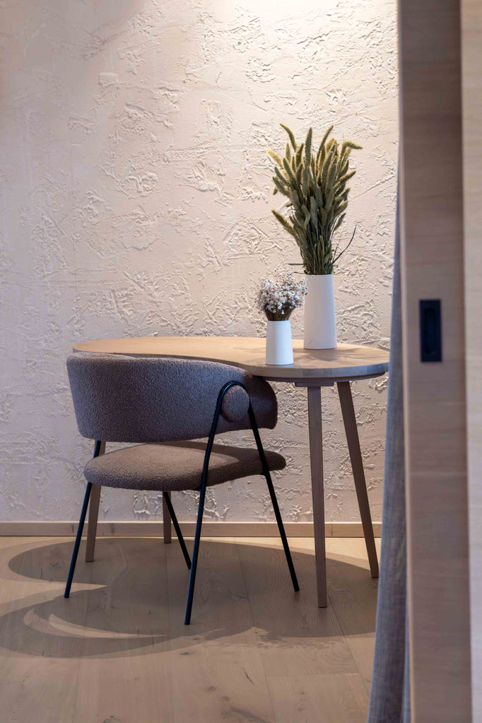 A cosy seating area with a modern armchair, a round wooden table and subtle floral arrangements at the PETRUS boutique hotel in Reischach-Bruneck • South Tyrol, inviting guests to linger and relax.