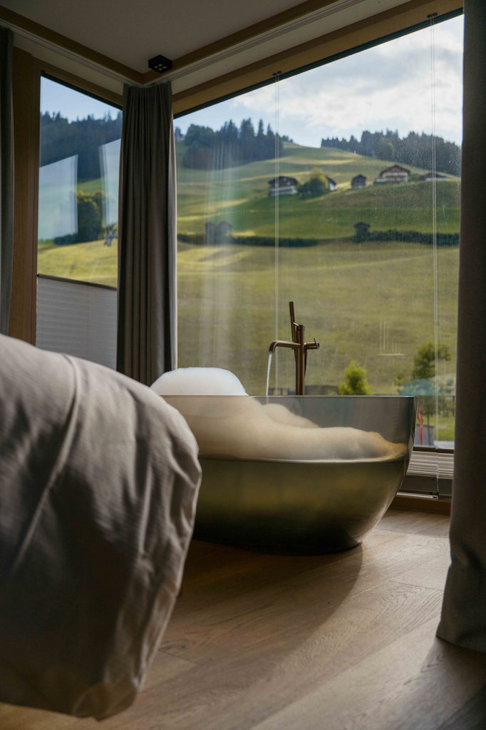Schlafzimmer mit freistehender Badewanne vor dem Panoramafenster in einer Suite des 5 Sterne Wellnesshotel Nesslerhof in Großarl