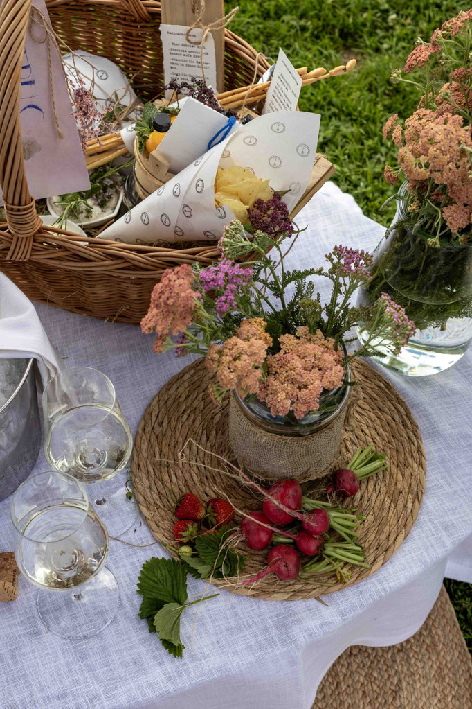 Detailaufnahme eines Picknicktisches mit Blumen, regionalen Spezialitäten, frischem Gemüse und Wein im Garten des Boutiquehotel PETRUS in Reischach-Bruneck • Südtirol, liebevoll arrangiert für einen genussvollen Aufenthalt in der Natur.