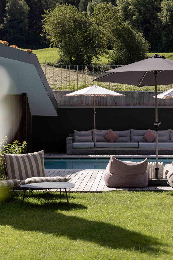 Außenpool mit gemütlichen Loungemöbeln, Sonnenschirmen und Blick auf die grüne Landschaft rund um das Boutiquehotel PETRUS in Reischach-Bruneck • Südtirol.