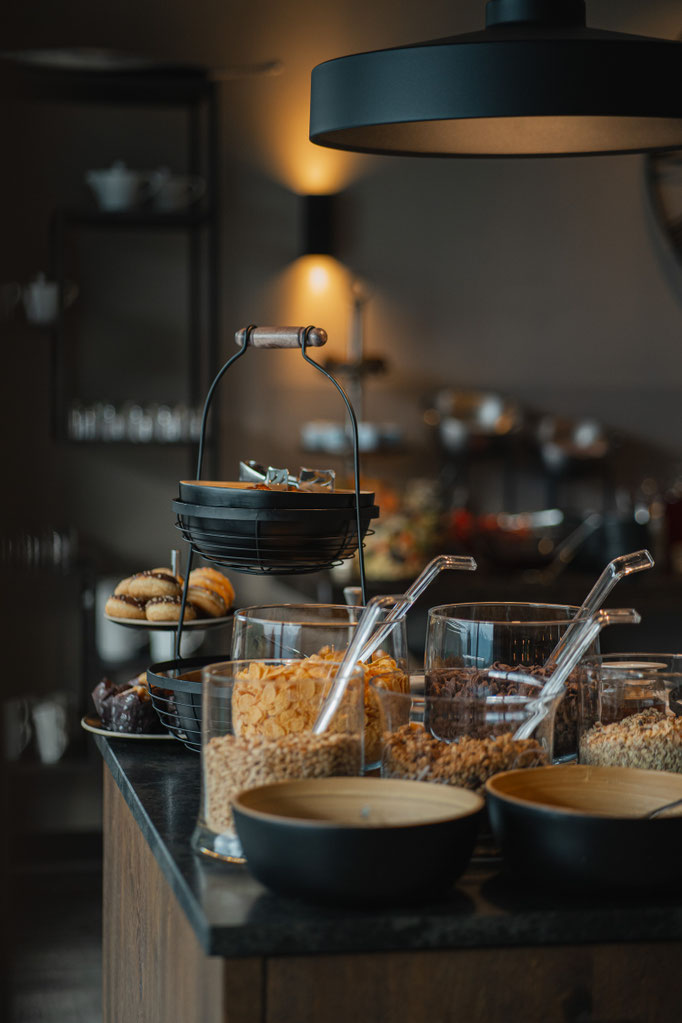 A close-up of the breakfast buffet at the Hotel Mair am Ort Living in Partschins near Merano in South Tyrol, featuring a variety of muesli, pastries and regional breakfast ingredients, served in a modern, stylish setting.