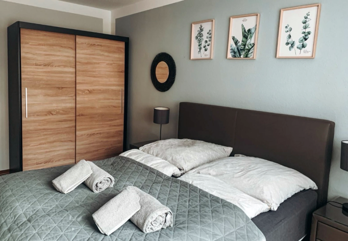 Gemütliches Schlafzimmer mit Doppelbett, stilvoller Wanddekoration und modernem Kleiderschrank in Holzoptik. Liebevoll gefaltete Handtücher und dezente Farben sorgen für eine entspannte Atmosphäre in unserer Ferienwohnung in Winterberg-Niedersfeld.