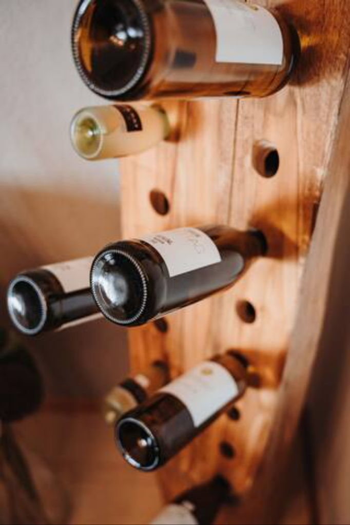 Nahaufnahme eines dekorativen Weinregals aus Holz mit mehreren liegenden Weinflaschen. Die schräg eingesetzten Flaschen machen das Regal zu einem stilvollen Blickfang mit rustikalem Charme – ideal für Weinliebhaber.