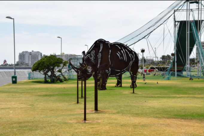 2016 | Kapstadt | «Three Anchor Bay»: «Giganto-Eisenplastik». Durch ein Guckloch gesehen ergeben die 5 «Einzelteile» ein riesengrosses Nashorn. Eine Super-Idee!