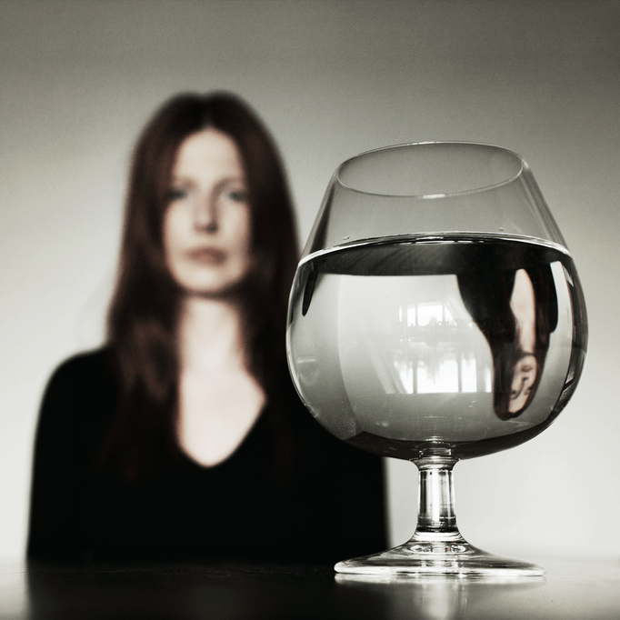 Manuela Deigert Bildsprache Frau sitzt an einem Tisch und wird in einem Cognacglas reflektiert