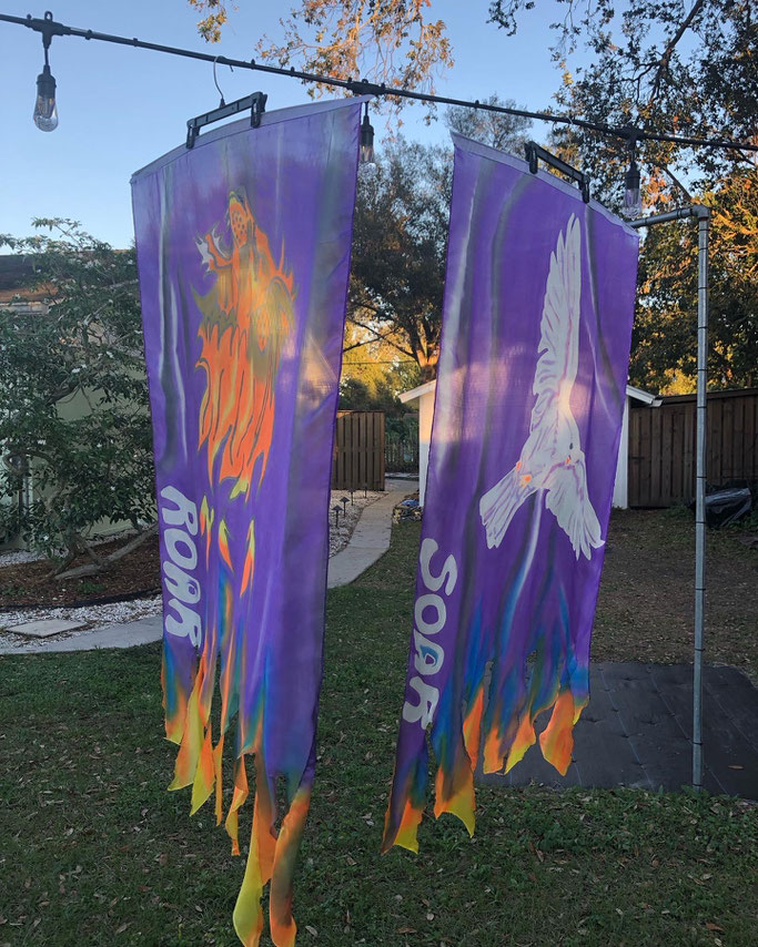 Set of flags, one with a roaring lion, "Roar" - the other with a flying dove, "Soar". There are  flames on the ends of the flags.