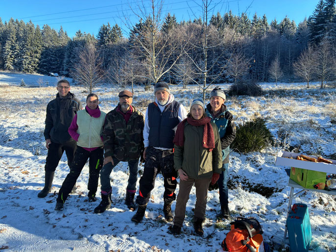 6 Menschen stehen im Vordergrund während dahinter eine vereiste Landschaft mit Häufen an Verbuschungsmaterial zu sehen ist.