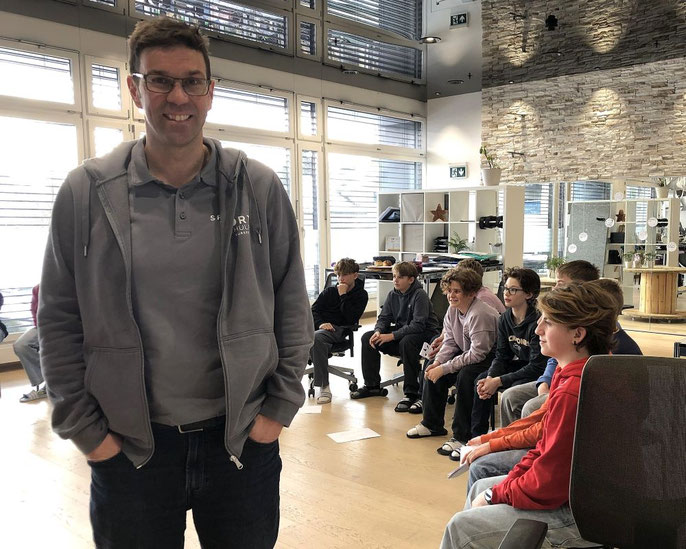 Portraet_Peter_Bigler_Leiter_Sportschule_Sursee_in_Klassenzimmer_Lernende_sitzen_hinter_ihm_Kreis