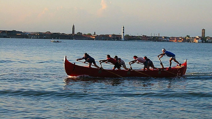 Ruderboot mit fünf Personen auf den Gewässern von Albarella, umgeben von Natur und historischen Türmen der Umgebung.