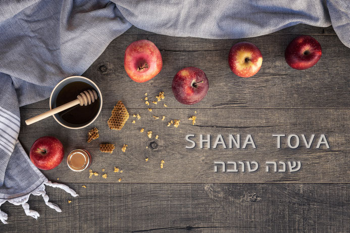 Äpfel und Honig auf einem Tisch sowie der Schriftzug Shana Tova