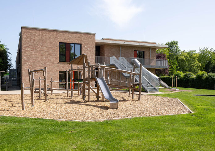 Neubau Kita Bergheim-Ahe, Kinderperspektive mit Blick auf Spielgeräte, Rutsche und Gebäude