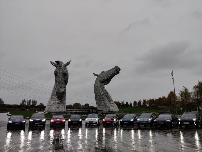 2 Volkswagen, 1 Kia und 7 Teslas stehen vor zwei Pferdekopf-Statuen.