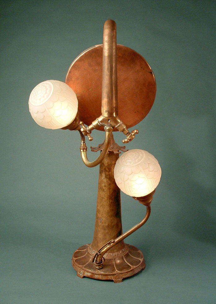 Assemblage light art sculpture made from brass and copper pieces and art deco glass. The brass and copper pieces include a faucet turned upside down, a musical instrument bell, and a pan from a balance scale.