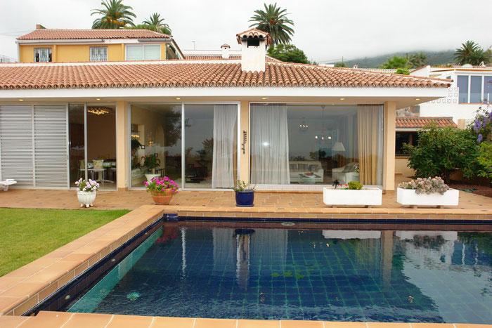 Cristalblaues Wasser im Pool vor der Villa mit großen Schiebefenstern.