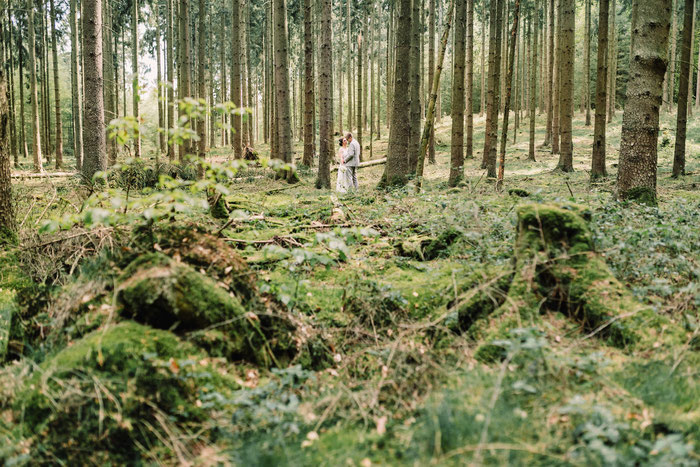 Ein Traupaar in unweiter Ferne im Wald, Moos im Vordergrund des Bildes