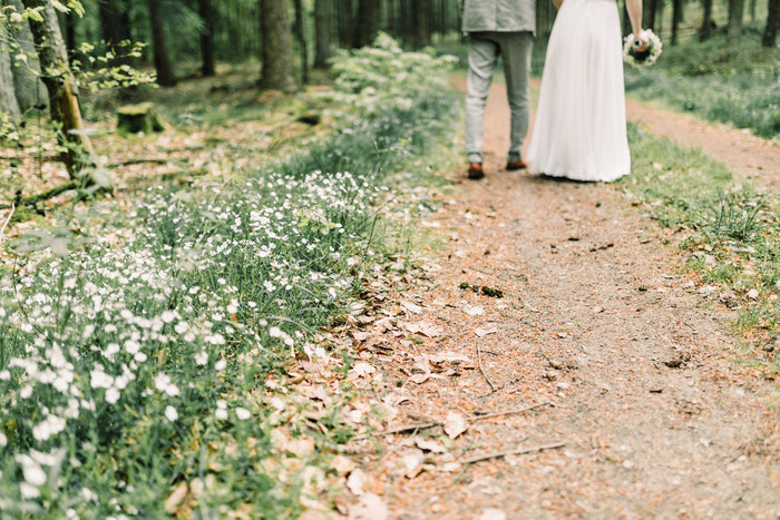 Hochzeitspaar läuft auf einem Waldweg, Blumen wachsen am Wegesrand