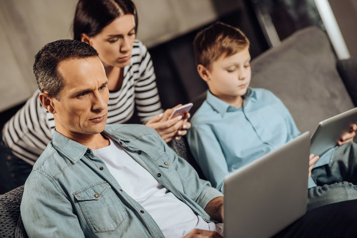 eine Familie im Wohnzimmer, alle starren auf unterschiedliche Medien