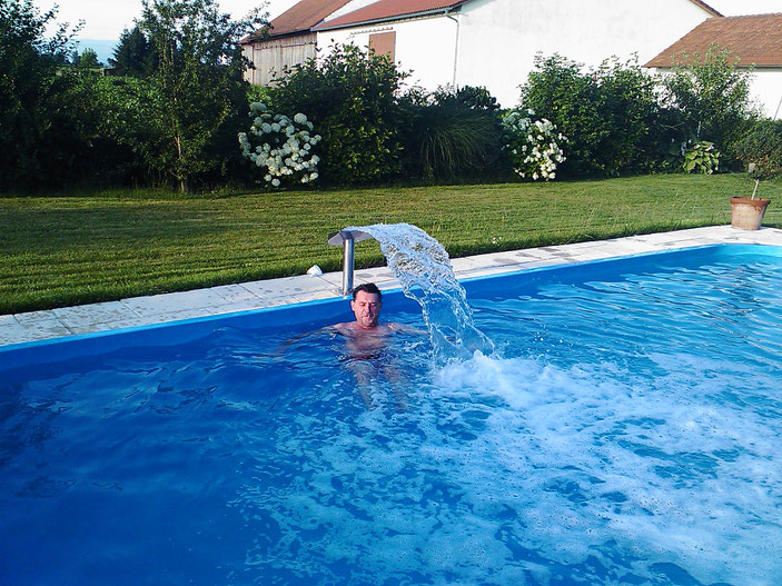 Mann steht im Pool unter einer Nackendusche