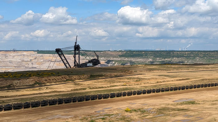 Blick vom Hambacher Forst in den Braunkohlentagebau im Mai 2024. Im Hintergrund die Kohlekraftwerke, in denen die Braunkohle verbrannt wird - aber auch Windenergieanlagen als Zeichen des Strukturwandels im Revier. Foto: Herbert Antweiler.