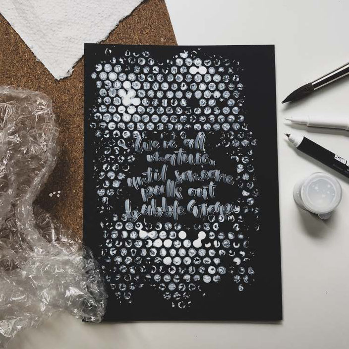 Handlettering in weiss auf schwarz mit einem Hintergrund aus Noppenfolie: We're all mature, until someone pulls out bubble wrap