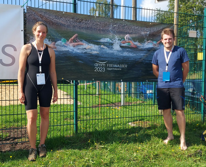 Rebecca Kiefer und Paul Feldmann vor dem Plakat der Freiwassermeisterschaften.