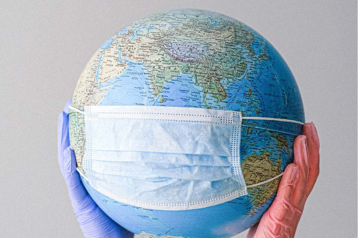 Von zwei Händen hochgehaltener Globus mit medizinischer Maske darüber