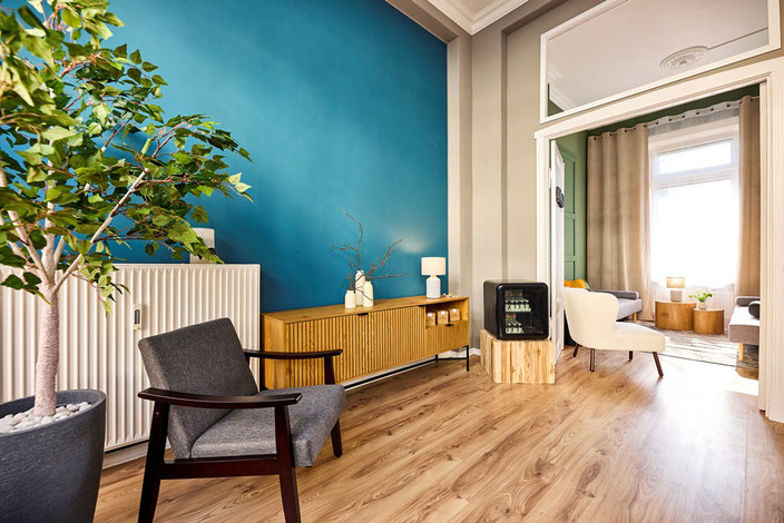 Stress ausblenden dank Entspannung: Das Bild zeigt die Innenräume des NORDIC RELAXING-Studios in Lübeck. Im Vordergrund steht ein schwarzer Stuhl, ein Baum und eine Kommode. Im Hintergrund öffnet sich ein zweiter Raum.
