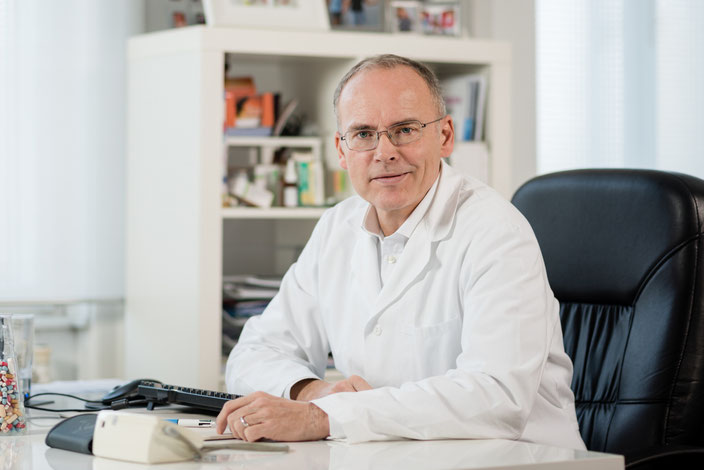 Dr. Marcus Franz, Internist in Hietzing am Schreibtisch im weißen Arztkittel