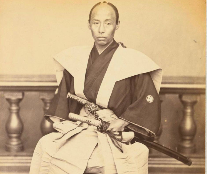A vintage photograph of a samurai in traditional attire, wearing a formal kimono with family crests and holding two swords (daisho).