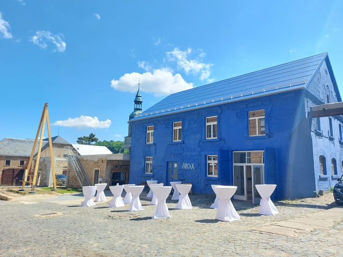 Blaues Haus mit weißen eleganten Stehtischen davor 