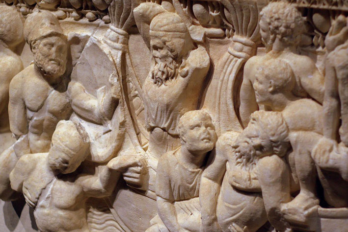 Close-up of an ancient marble relief showing expressive human figures in motion, carved in high detail.