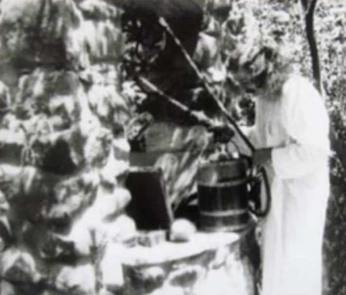 Meher Baba drawing water from the bucket at the well at Harmon