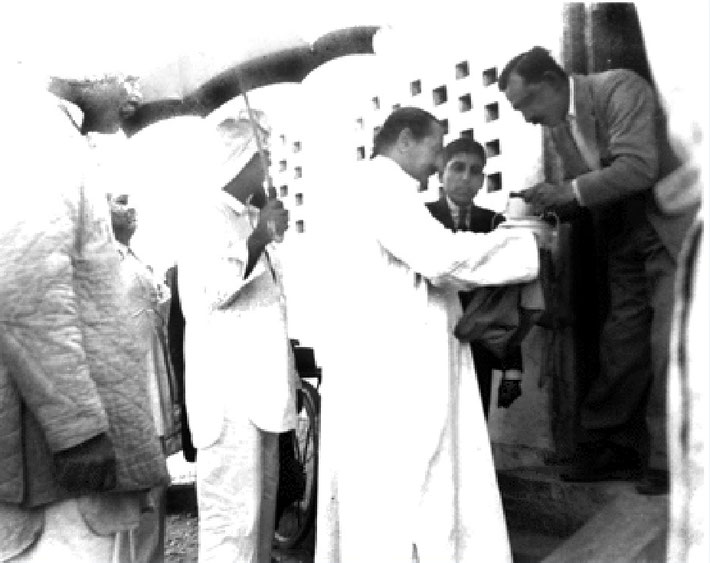 Meher Baba accepting "bhiksha"  from Keki Nalavala during the New Life. Elcha Mistry is looking on.