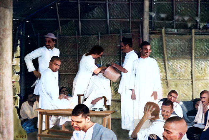 13. 1938 : Meherabad, India. Meher Baba caring for a group of Masts, with Pleader ( light hat ) & Baudul ( bucket ) assisiting him. Mohammed Mast standing smiling.