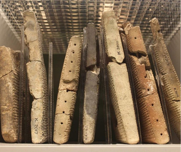 Ancient clay tablets with cuneiform writing are stored upright behind glass, showcasing early written records.