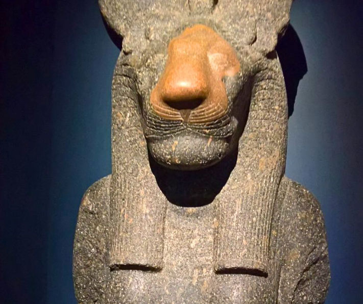 A statue of the lion-headed Egyptian goddess Sekhmet, crafted from dark stone, displays detailed features and a serene expression, symbolizing her dual role as a protector and a bringer of wrath.