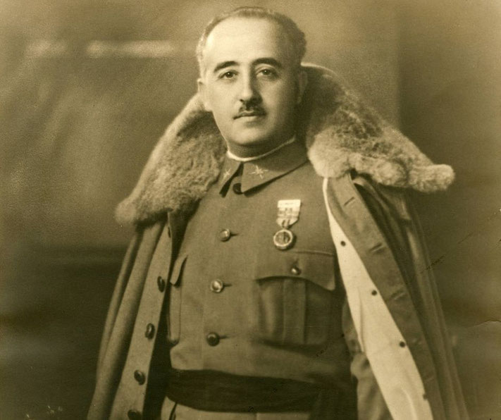 A man in military uniform poses formally, wearing a coat with a fur collar draped over his shoulders and medals on his chest, looking directly at the camera.