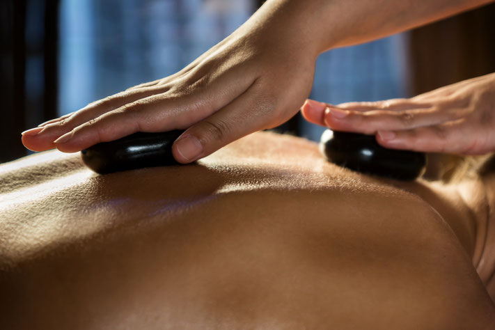 Ein Therapeut führt mit warmen, glatten schwarzen Steinen eine entspannende Rückenmassage bei einem Kunden durch.