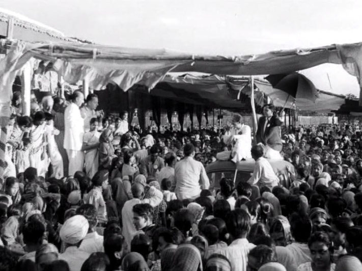 Ahmednagar, India ; 1954. Meher Baba atop of a car paraded through the crowds, whilst the Western men look on from the left of screen