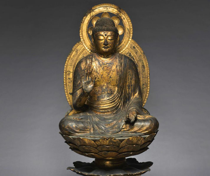 A gilded Buddha statue sits in a meditative pose on a lotus pedestal, with a radiant halo behind.