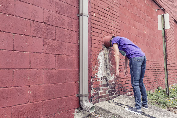 Eine Frau steckt ihren Kopf in ein Rohr in der Wand.