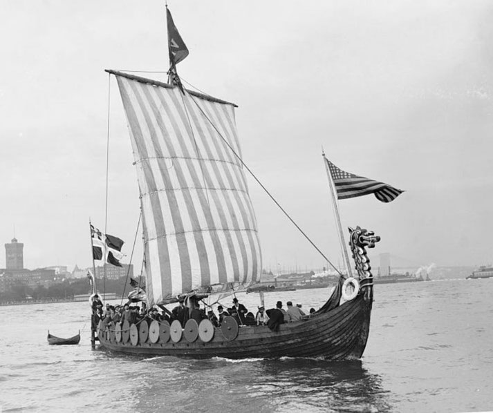A replica Viking longship with a striped sail, round shields along the sides, and a dragon-headed prow.