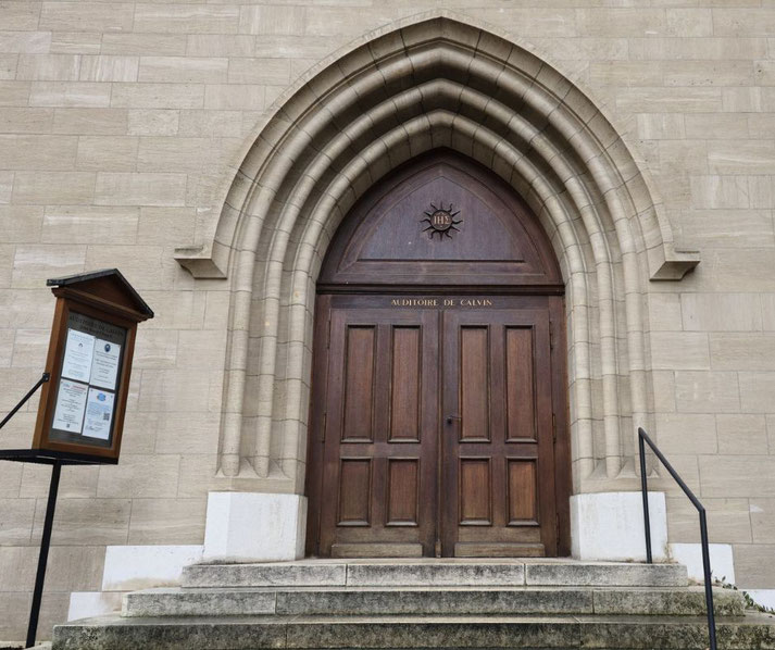 The entrance of the Auditoire de Calvin in Geneva, a historic Reformation-era building. The wooden doors, Gothic arch, and plaque highlight its significance as a Protestant teaching site.