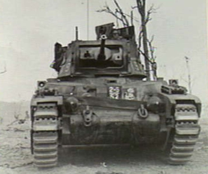 A front-facing view of a World War II-era tank on barren terrain, with a soldier visible in the turret.
