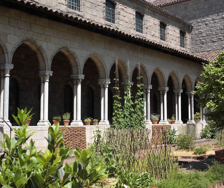 A medieval-style cloister with arched stone columns surrounding a lush garden.