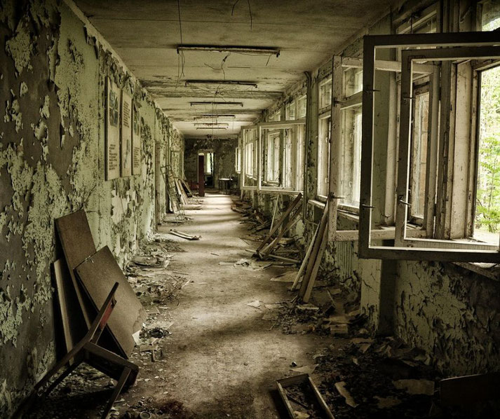 Decaying hallway with peeling paint, broken furniture, and open windows letting light into the abandoned building.