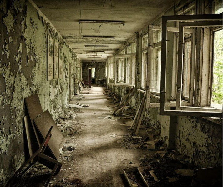 Decaying hallway with peeling paint, broken furniture, and open windows letting light into the abandoned building.