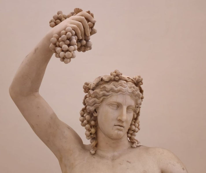 Marble statue of a youthful figure with grapes in hair, holding a bunch of grapes aloft, symbolizing festivity and wine.